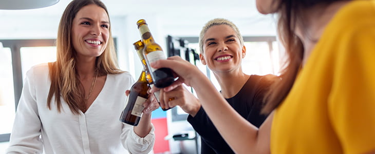 Three businesswomen toast bottles of beer at a Happy Hour event